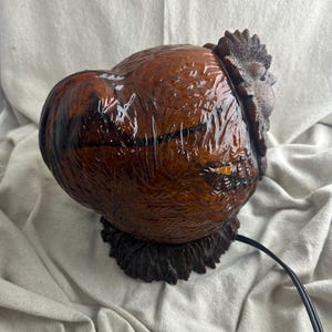 May include: A brown rooster-shaped lamp with a glossy finish. The lamp features a detailed textured design, including the rooster's comb and feathers. The lamp sits on a dark brown base and has a black power cord.