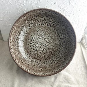 May include: A large, brown ceramic bowl with a speckled glaze. The bowl has a wide, round shape and a smooth, glossy finish.