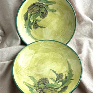 May include: Two round ceramic bowls featuring a hand-painted yellow wash background with visible brushstrokes. Each bowl is decorated with a detailed green artichoke illustration and finished with a solid dark green rim along the edge.