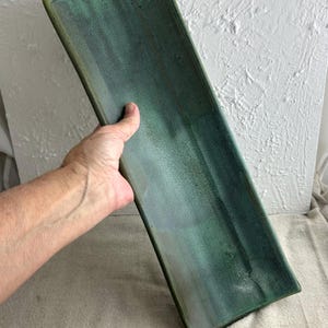 May include: Rectangular ceramic serving platter with a gradient of green and teal hues. The edges are slightly raised and a darker green. The platter is held by a hand, showcasing its size and shape. Ideal for serving appetizers or displaying decorative items.