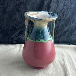 May include: A small, red ceramic vase with two handles. The vase has a green, blue, and white glaze on the top.