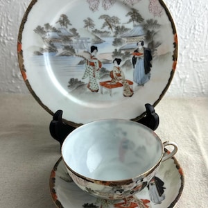 May include: A vintage Japanese tea set with a delicate floral design. The set includes a cup, saucer, and a larger plate with a scene of women in traditional clothing.