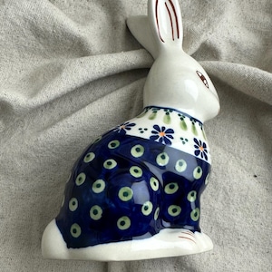 May include: A ceramic bunny figurine with a white head and ears, and a blue body adorned with green and white floral patterns. The bunny is sitting upright, showcasing its detailed design. A decorative piece for Easter or spring.