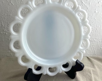 May include: A white milk glass plate with a scalloped edge. The plate is on a black stand.