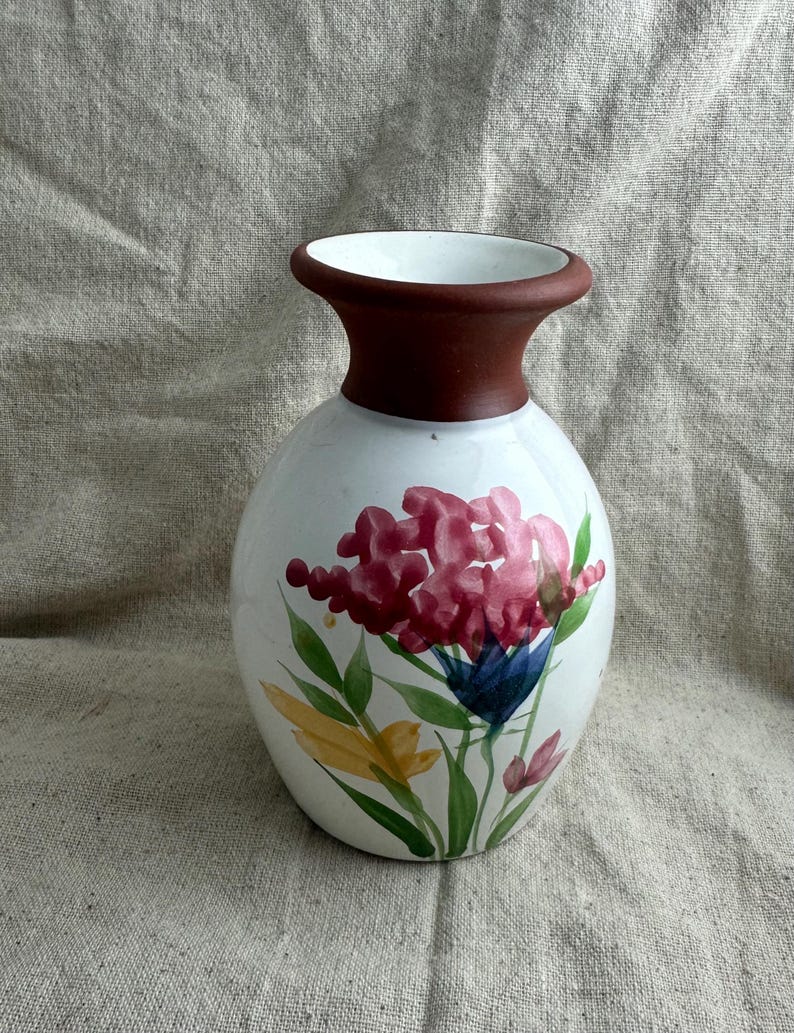 Puede incluir: Jarr&oacute;n de cer&aacute;mica blanca con cuerpo bulboso y cuello marr&oacute;n oscuro. El jarr&oacute;n est&aacute; pintado a mano con un dise&ntilde;o floral con flores rosas, azules y amarillas con hojas verdes. Una pieza decorativa para la decoraci&oacute;n del hogar.