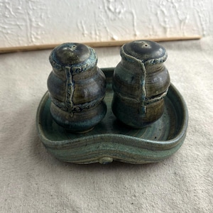 May include: A set of two blue and brown ceramic salt and pepper shakers with a matching blue and brown ceramic tray.