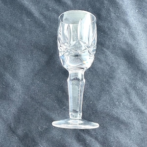 May include: A clear glass shot glass with a cut crystal design. The glass has a tall, slender stem and a round base.