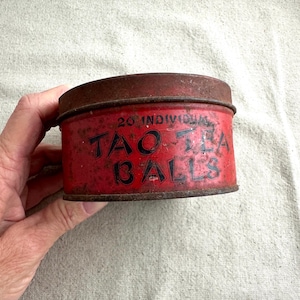 May include: A red metal tin with the text "20 INDIVIDUAL TAO TEA BALLS" printed in black. The tin is slightly rusted and has a worn appearance.