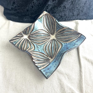 May include: A blue ceramic dish with a wavy edge and a raised floral design. The dish has a light blue glaze with brown accents.