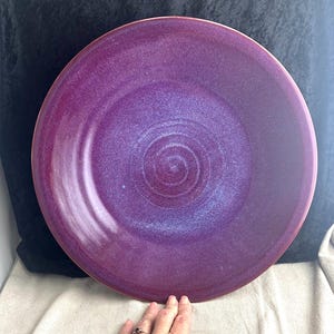 May include: A large, round, purple ceramic serving bowl with a swirling pattern. The bowl has a glossy finish and is handmade.