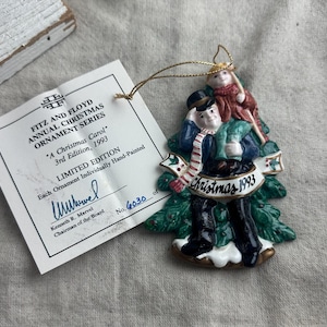 May include: A Fitz and Floyd Christmas ornament from the "A Christmas Carol" series, 3rd Edition, 1993. The hand-painted ornament features a man and child figure on a Christmas tree base, with the text "Christmas 1993". Includes a tag.