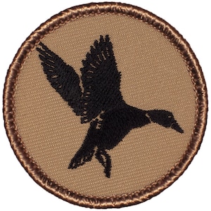 May include: A brown embroidered patch with a black silhouette of a bird in flight.