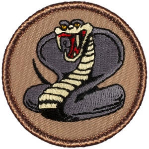 May include: A brown embroidered patch with a gray cobra with yellow eyes and a red mouth. The cobra is in a coiled position with its head raised and fangs bared.