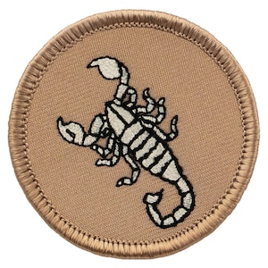 May include: A tan embroidered patch with a white scorpion design. The scorpion is facing right and has a curled tail.