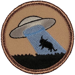 May include: A brown embroidered patch with a gray UFO beaming a blue light down on a black silhouette of a cow.