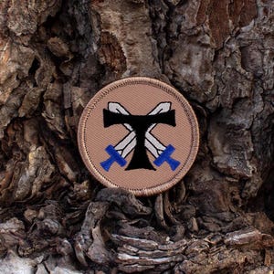 May include: A tan embroidered patch with a black cross and two swords. The swords are crossed and the handles are blue.