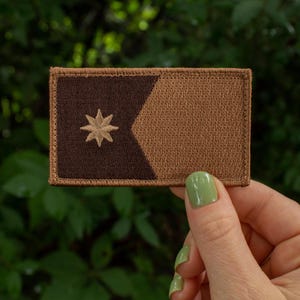 May include: A brown and black fabric patch with a five-pointed star in the center. The star is a light brown color.