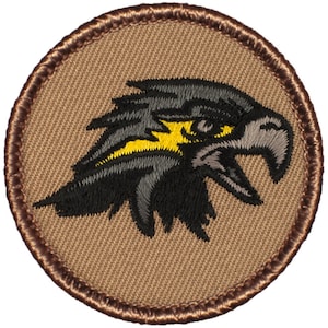 May include: A brown embroidered patch with a black and yellow eagle head design. The eagle has a yellow beak and yellow eyes.