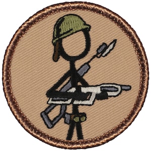 May include: A brown embroidered patch with a stick figure soldier wearing a green helmet and holding a rifle. The background is a tan fabric.