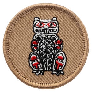 May include: A round, tan fabric patch with a white and black embroidered image of a stylized bear with red accents. The bear is sitting upright with its paws in front of it.