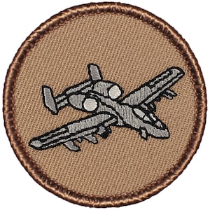 May include: A brown embroidered patch with a gray A-10 Thunderbolt II aircraft in flight.