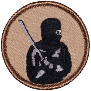 May include: A brown embroidered patch with a black silhouette of a ninja holding a silver sword. The ninja is wearing a black mask and a black hooded robe.