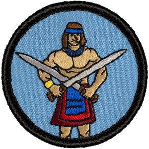 May include: Embroidered patch featuring a cartoon warrior holding two swords crossed in front of their chest. The warrior is wearing a blue and red kilt, a blue headband, and a necklace. The background is light blue.