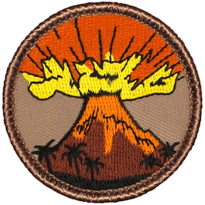 May include: Embroidered patch featuring a volcano erupting with orange and yellow flames against an orange sky. The volcano is brown with palm trees at the base, set on a tan background, and framed by a brown border.