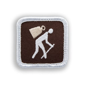 May include: A brown fabric patch with white stitching around the edges. The patch features a white silhouette of a person carrying a backpack and walking with a stick.