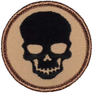 May include: A black embroidered skull patch on a tan background with a brown stitched border.