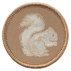 May include: Embroidered patch featuring a white squirrel with a red eye on a tan background. The squirrel is in a seated position, with detailed stitching. The patch has a tan border and is circular in shape.