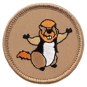 May include: A brown embroidered patch with a cartoon image of a beaver with orange fur, a white belly, and black eyes. The beaver is standing on its hind legs with its arms outstretched and a wide grin.