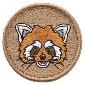 May include: A brown embroidered patch with a red panda face. The panda has white fur around its eyes and mouth, and green eyes.