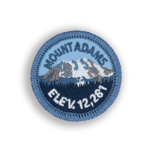May include: A blue and white embroidered patch with the text "Mount Adams Elev. 12,287" and a depiction of a mountain with snow on top.