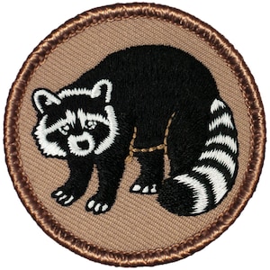 May include: A brown embroidered patch with a black and white raccoon on a tan background. The raccoon is facing left and has a white stripe on its face.
