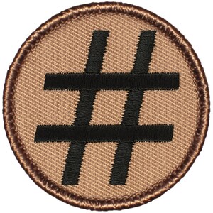 May include: A brown embroidered patch with a black hashtag symbol in the center.