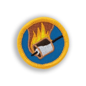May include: A blue and yellow embroidered patch with a marshmallow on a stick over a campfire.
