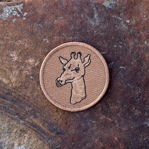 May include: A brown embroidered patch with a black outline of a giraffe's head.
