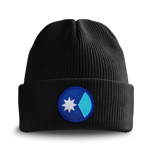 May include: Black ribbed knit beanie with a circular patch. The patch features a white star and a light blue diamond shape on a dark blue background. The beanie is a classic winter accessory.