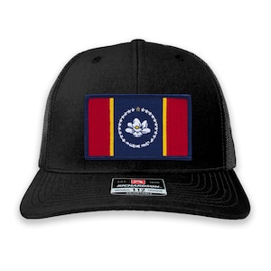 May include: Black trucker hat with a patch of the Mississippi state flag. The patch features a magnolia flower and the words "In God We Trust". The hat is adjustable and has a Richardson 112 logo.