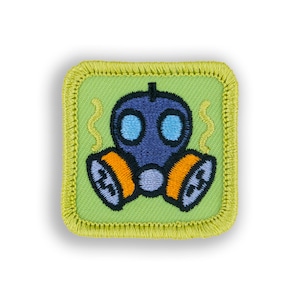 May include: A green embroidered patch with a blue gas mask with orange filters. The gas mask has two blue eyes and a black nose. There are yellow wavy lines around the gas mask.