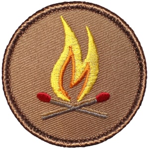 May include: A brown embroidered patch with a yellow and orange flame and two gray matchsticks with red tips.