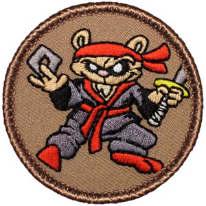 May include: A brown embroidered patch with a cartoon ninja bear wearing a red headband and holding a sword. The bear is wearing a gray ninja suit with a red sash.