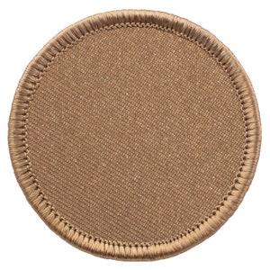 May include: A round, tan patch with a textured fabric center and a stitched border. The patch has a simple, minimalist design, suitable for various applications. The color is a warm, neutral tone.