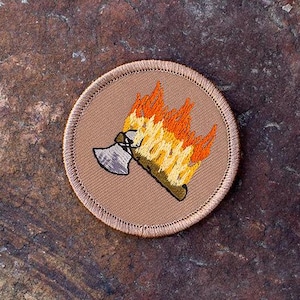 May include: A tan embroidered patch with a small axe engulfed in flames. The flames are orange and yellow.