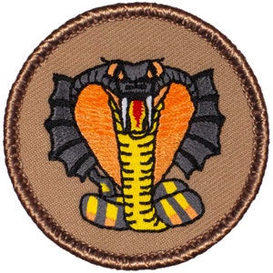 May include: Embroidered patch featuring a cobra with its hood raised, fangs bared, and a yellow and black striped body. The patch is circular and has a brown background with a brown stitched border.