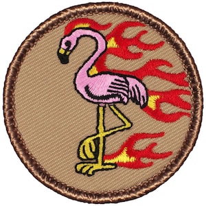 May include: A brown embroidered patch with a pink flamingo standing on one leg with yellow feet and a red and yellow flame design behind it.