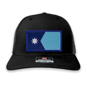 May include: A black trucker hat with a blue and light blue patch featuring a white star. The patch is sewn onto the front of the hat. The hat has a black mesh back and an adjustable strap with a black label that reads "Richardson 112 Original Trucker Adjustable".