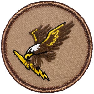 May include: Embroidered patch featuring a brown eagle with yellow accents, clutching a yellow lightning bolt. The eagle has a white head and is set against a tan background, framed by a brown stitched border. A military or aviation-themed design.