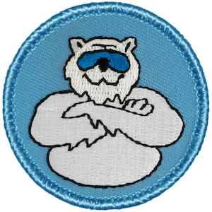 May include: A white embroidered patch with a cartoon yeti wearing sunglasses. The yeti is standing with its arms crossed and has a blue background. The patch is surrounded by a blue border.